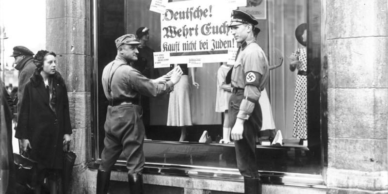 An den Fenstern jüdischer Geschäfte werden von Nationalsozialisten Plakate mit der Aufforderung "Deutsche, wehrt euch, kauft nicht bei Juden" angebracht.